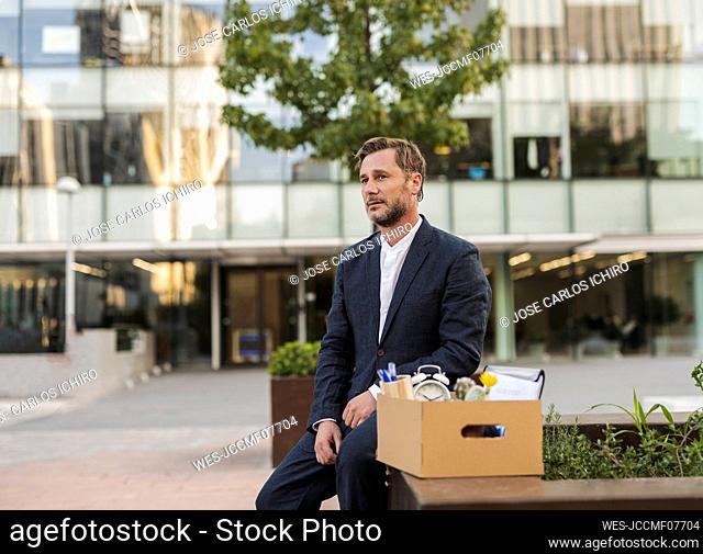Sad businessman sitting with cardboard box outside office building