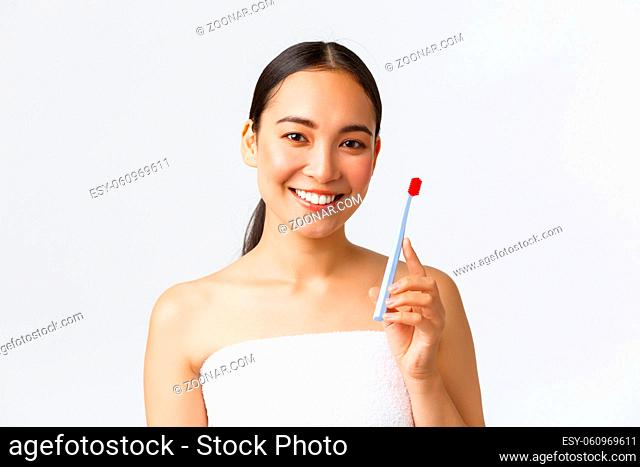 Beauty, personal care, and hygiene concept. Close-up of beautiful healthy asian girl in bath towel, showing toothbrush, promo of teeth treatment supplies