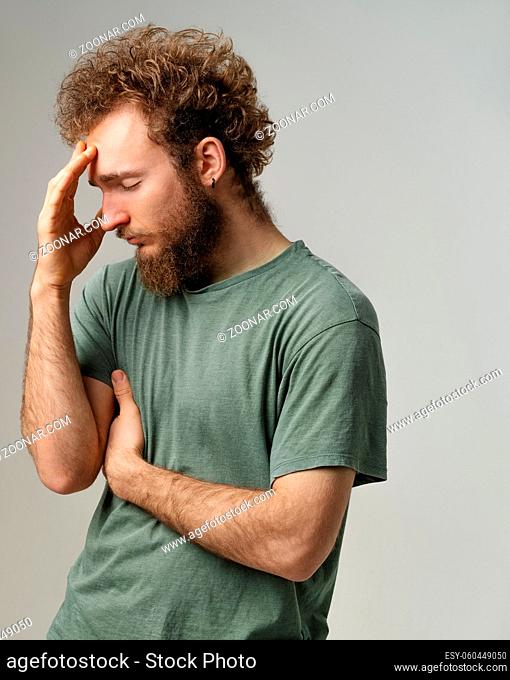 Has a headache or shame for an opponent young man touching his forehead. Handsome young man with curly hair in olive t-shirt isolated on white background