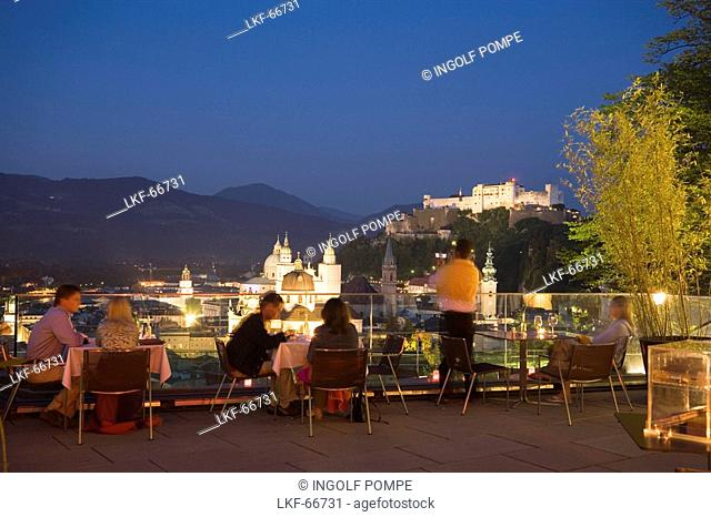 People sitting on terrace of the restaurant Moenchsberg 32 in the evening, view over old town with Hohensalzburg Fortress, Salzburg, Salzburg, Austria