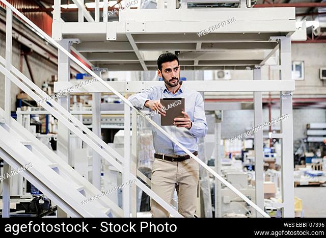 Contemplative businessman standing with tablet PC on staircase