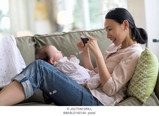 Asian mother taking cell phone photograph of baby in living room
