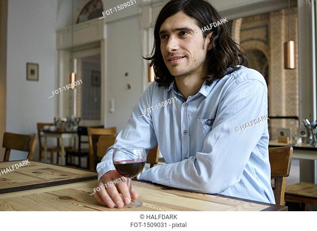 Smiling man having wine while sitting at cafe