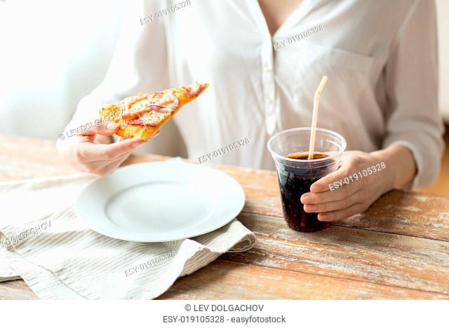 fast food, people and unhealthy eating concept - close up of woman hands with pizza and cola drink sitting at table