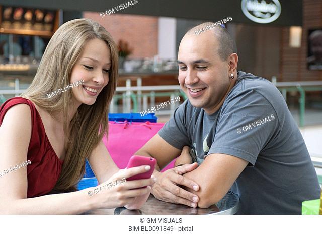 Hispanic couple sitting in cafe looking at cell phone