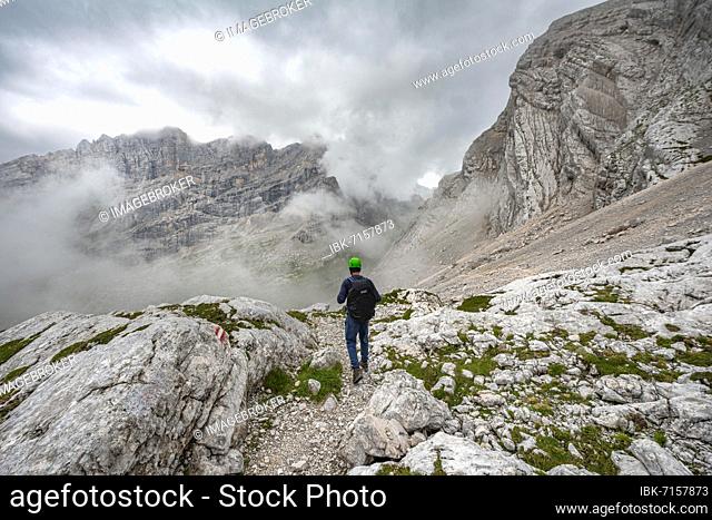 Hiker, climber on a trail between rocky cloudy mountains at Forcella Sore de la Cengia, Sorapiss circumnavigation, Dolomites, Belluno, Italy, Europe