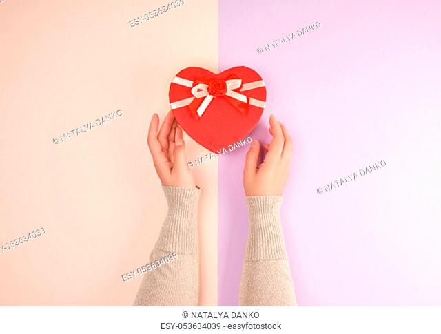 two hands hold a paper closed red box in the shape of a heart, festive backdrop