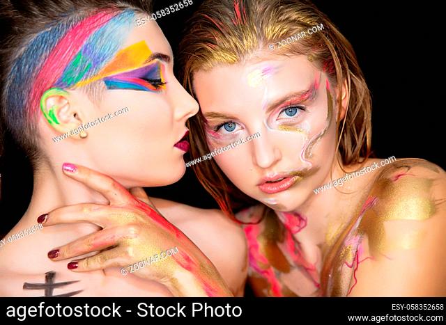 Two sexy young women with creative make-up on the face posing in the studio