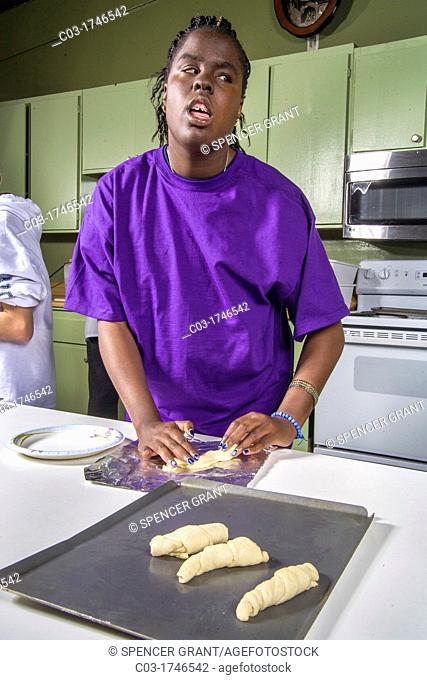 A blind African-American preteen girl makes rolls by touch from prepared dough in a cooking and baking class at the Blind Children's Learning Center in Santa...