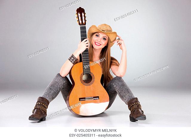 The beautiful girl in a cowboy's hat and acoustic guitar on a gray background