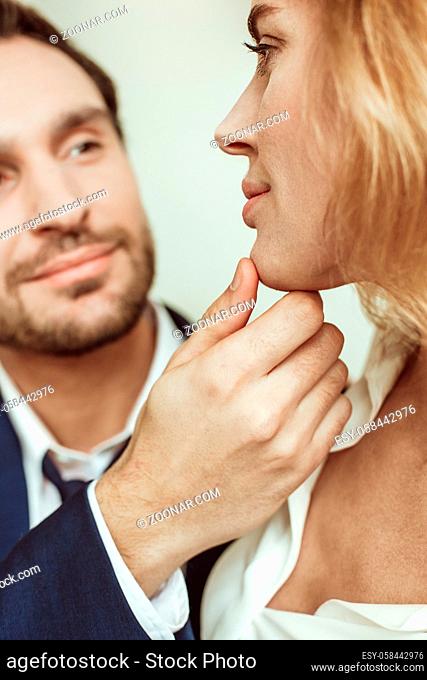 Close up portrait of passionate couple looking each other. Man touching female face. Selective focus on male hand and sexy blonde profile in foreground
