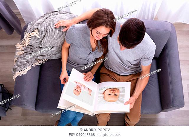 High Angle View Of An Couple Sitting On Sofa Looking At Photo Album