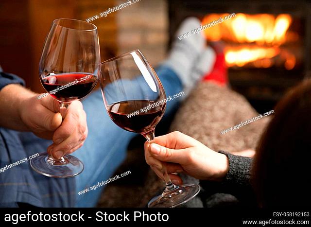 Couple in love sitting in a cozy room with fire place on a sofa with glass of wine. Family and love concept