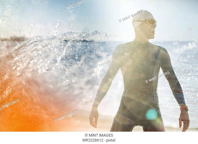 A swimmer in a wet suit standing by the water's edge