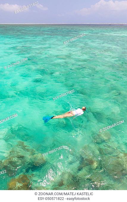 Woman snorkeling in clear shallow sea of tropical lagoon with turquoise blue water and coral reef, near exotic island. Mnemba island, Zanzibar, Tanzania