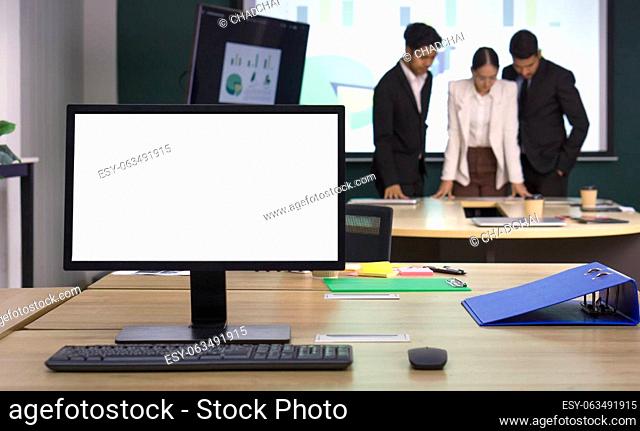 Blank screen desktop pc computer monitor on the desk. Business partners meeting in the background. Working atmosphere in a modern office
