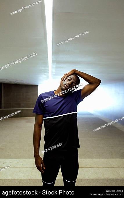 African man with eyes closed standing in underground stretching neck