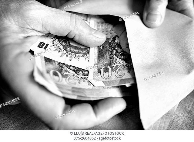 Woman hands putting banknotes pounds in an envelope
