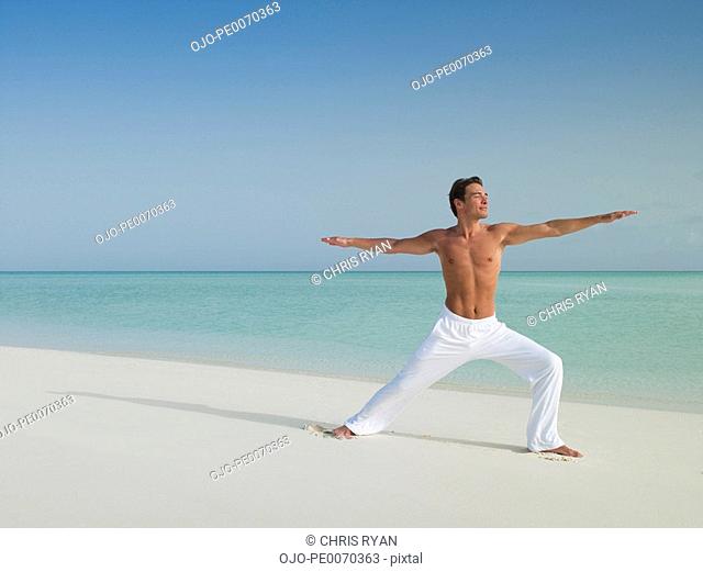 Man in warrior 2 yoga pose on beach