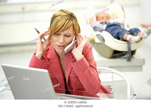 A business woman feels annoyed by the crying of her baby in her bureau. - DRESDEN, GERMANY, 23/08/2005
