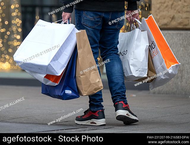07 December 2023, Hesse, Frankfurt/Main: A man walks along the Zeil in Frankfurt with full shopping bags in his hands. Christmas sales have started in the...