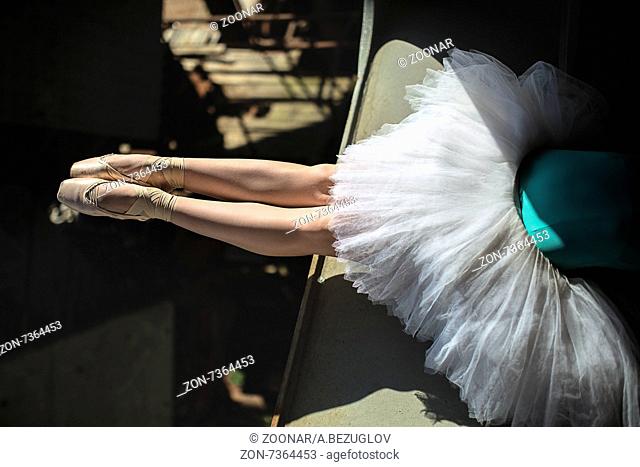 Ballerina sitting on the edge of the bridge. Feet shod with pointe. Dancer wearing a white tutu and blue swimsuit