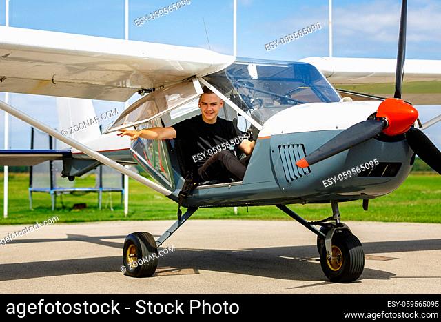 handsome teenage man sitting in small plane cockpit. young pilot closing door before take off. outdoor shot