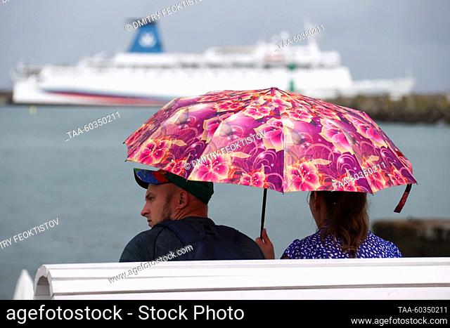 RUSSIA, SOCHI - JULY 9, 2023: A couple with an umbrella rest on a bench as rain falls over the Mayak beach. Last night's storm brought some 80mm of rain to...