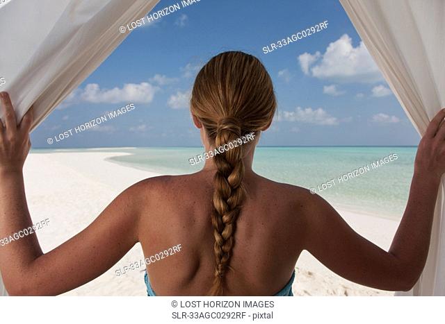 Woman admiring beach through curtains