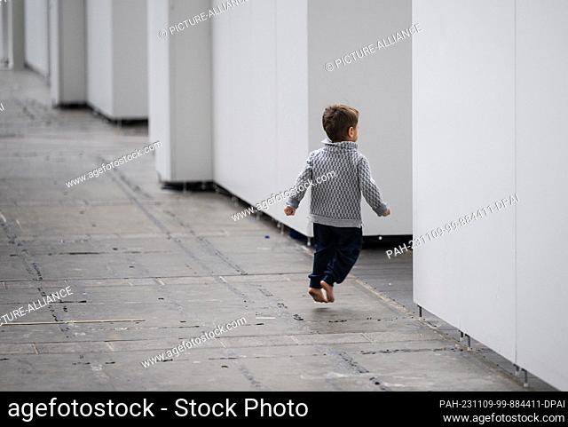 09 November 2023, Hesse, Frankfurt/Main: A young refugee boy walks barefoot across the concrete floor of the exhibition hall in Frankfurt