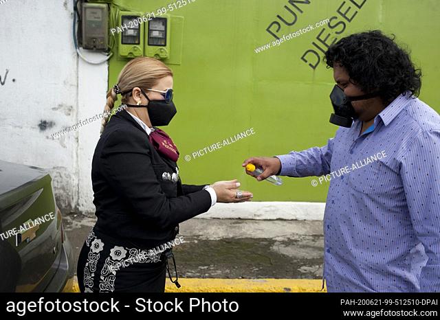 21 June 2020, Ecuador, Quito: One man hands disinfectant to a musician of the Mariachi group ""Mariachis a la Mexicana""