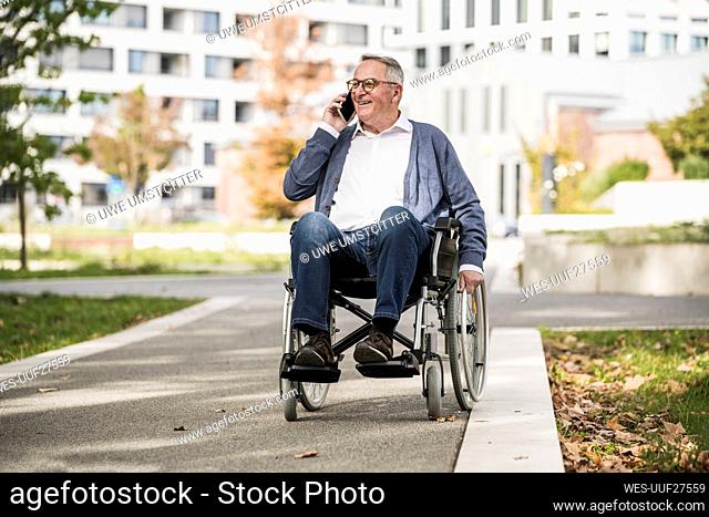Smiling senior man talking on mobile phone sitting on wheelchair