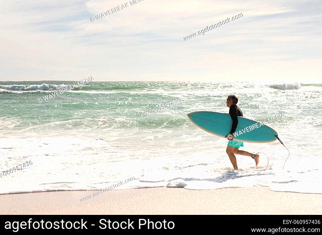 Side view of biracial senior man running with surfboard on shore at beach during sunny day