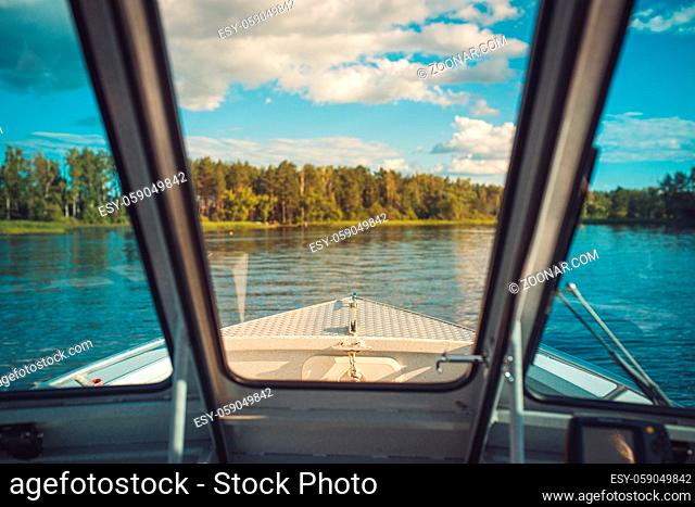 view from the boat cockpit cabin to the river expanse and a wooded shore with a blue cloudy sky