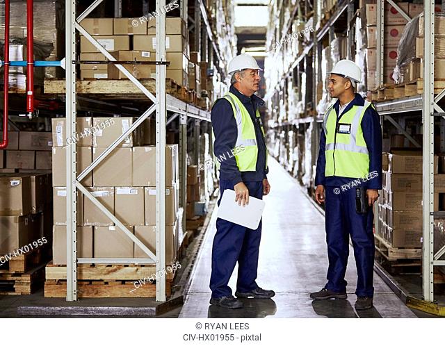 Manager and worker talking in aisle of distribution warehouse