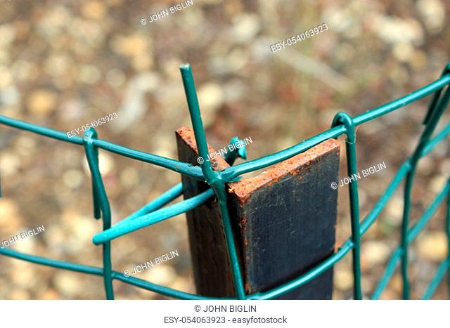 Metal mesh green wire fence on an angled iron post with one wire in a dangerous position, pointing upward with a background of blurred bark mulch