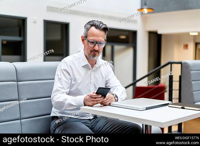 Male entrepreneur using mobile phone while sitting by table in office