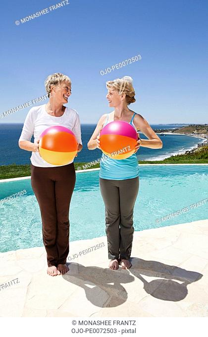 Senior women holding multicolor beach balls at poolside overlooking ocean