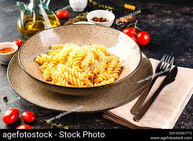 Cooked fusilli pasta in plate before adding cheese and sauce on dark background. Top view or flat lay