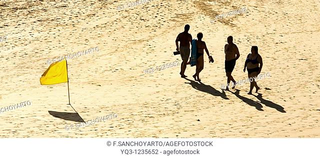 Vacationers walking by a yellow flag. Oriñon Beach, Castro Urdiales, Cantabria, Spain