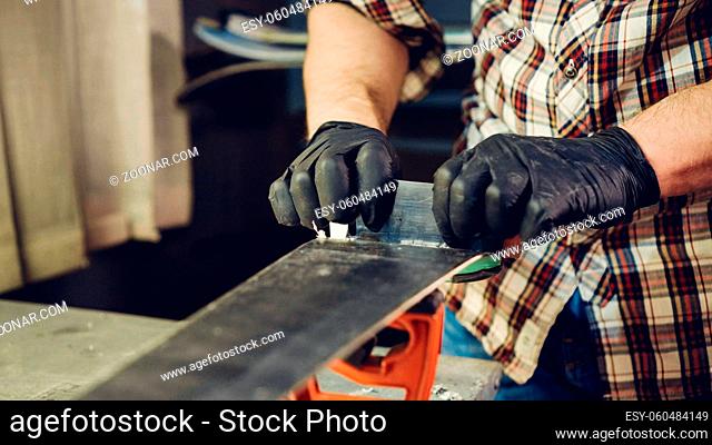 Ski maintenence. Removing excess wax from race ski base plastic scraper. Ski service and repair. Winter shop worker doing base repair