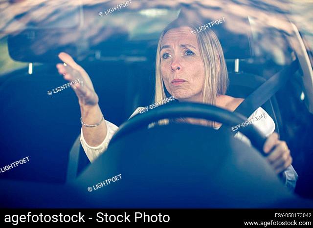 Middle aged woman at the steering wheel of her car, getting angry