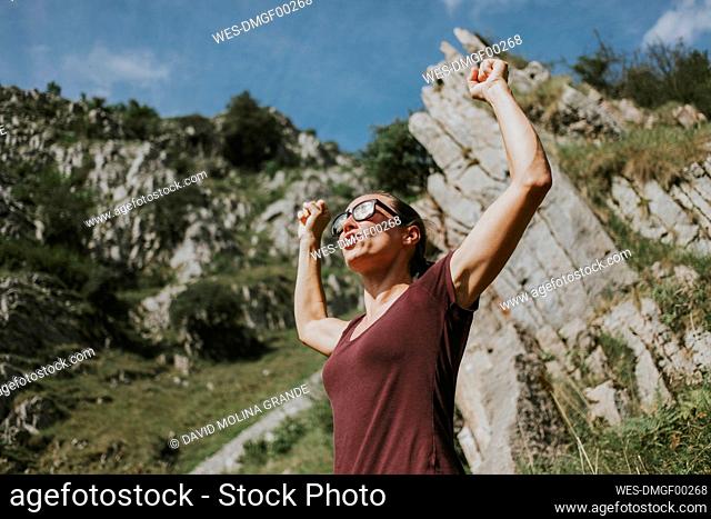 Woman celebrating victory with arms raised against mountain on sunny day