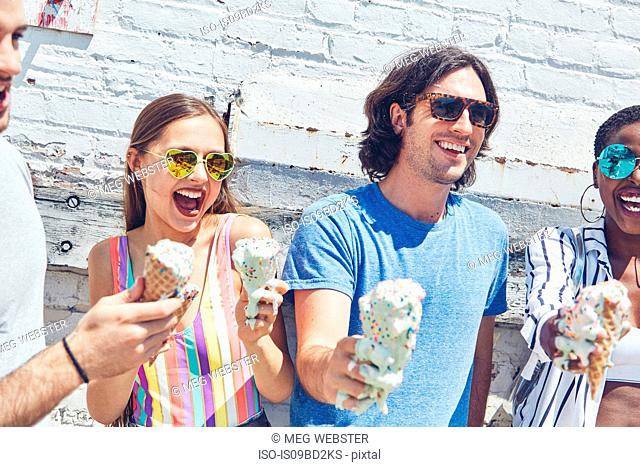 Young women and men holding melting ice cream cones, laughing