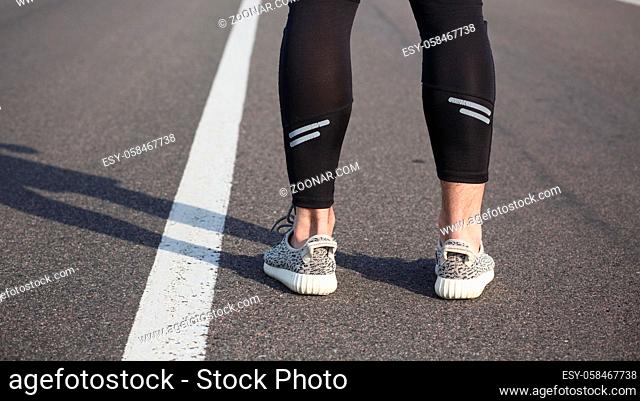 Closeup of male in running shoes going for run on road at sunrise or sunset. Man#39;s legs in jogging shoes on road near park