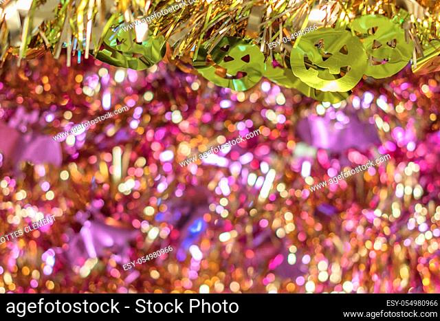 Background texture full of purple bokeh with golden garlands decorated by funny jack-o'-lantern pumpkin smiling faces decorations in foreground to celebrate the...