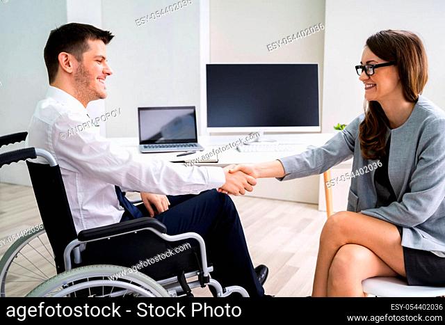 Businesswoman In Wheelchair Shaking Hands With Her Colleague In Office