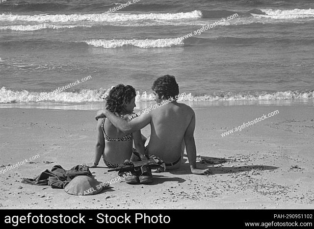 An Israeli soldier sits with his girlfriend on Tel Aviv beach, bathing in the sea, withtelmeer, private, soldier's boots