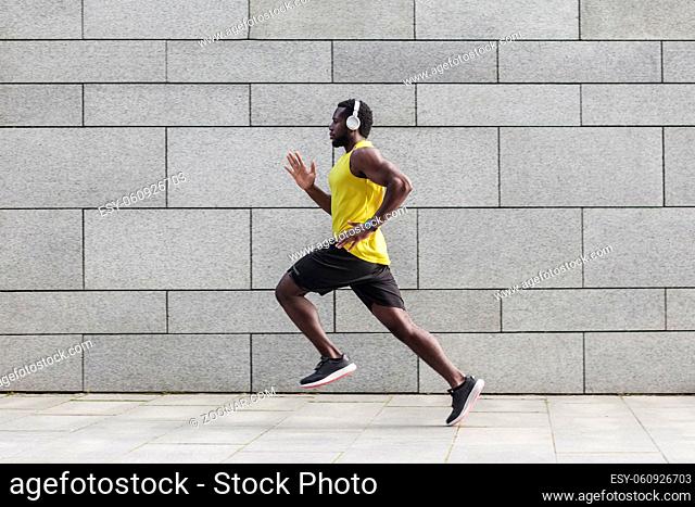 Profile portrait of adult male runner with muscular body in tracksuit jogging against gray wall with copy space area for text message or content