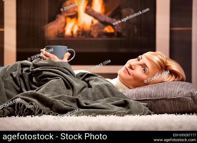 Woman resting at home lying on floor in front of a fire place